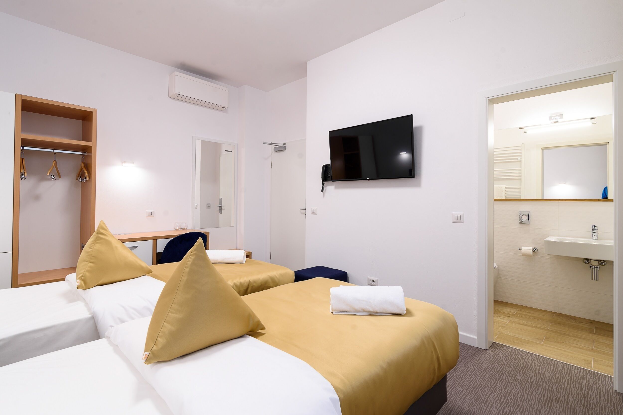 Ein Hotelzimmer mit zwei Betten, einem Fernseher, einem Spiegel, einem Kleiderschrank und einem Badezimmer.