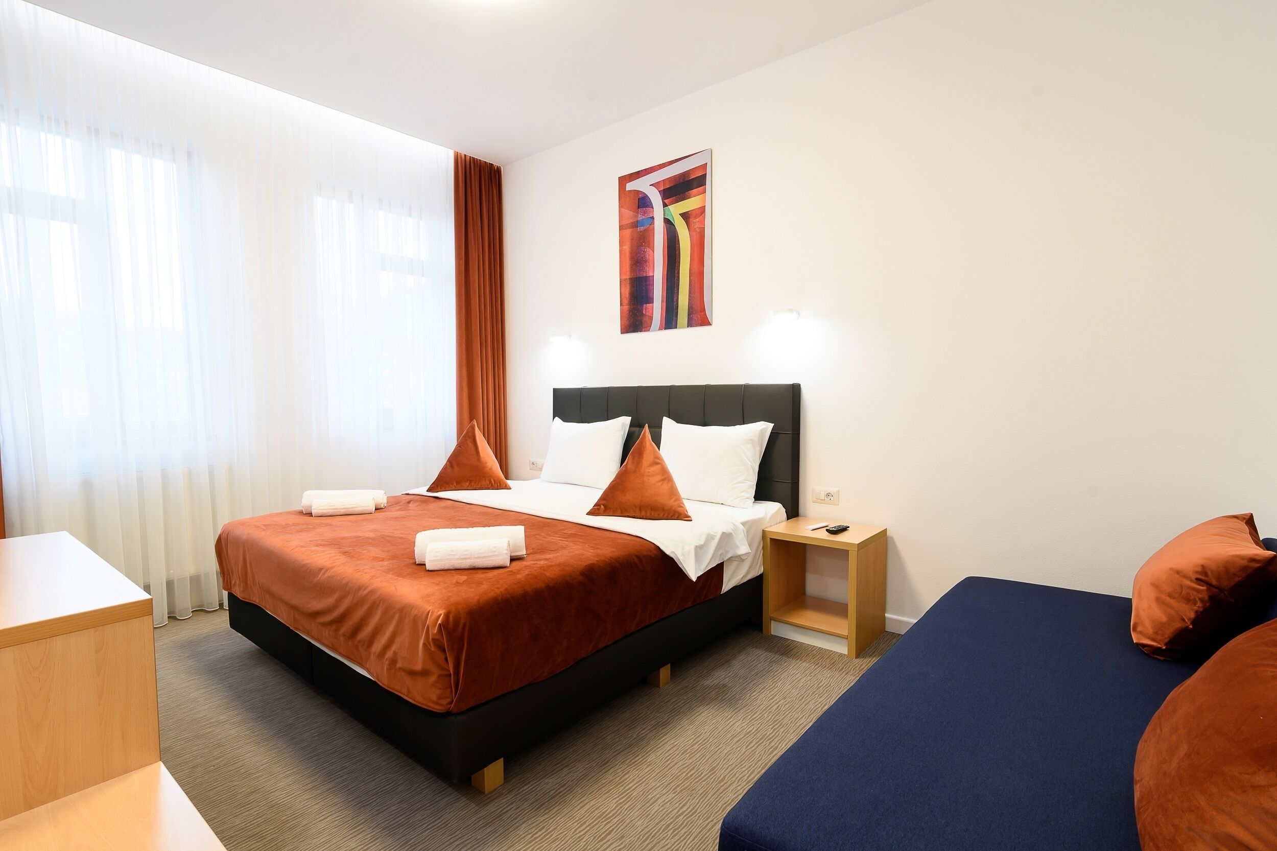 Una habitación de hotel con una cama grande, una cama más pequeña, un escritorio y una mesita de noche.