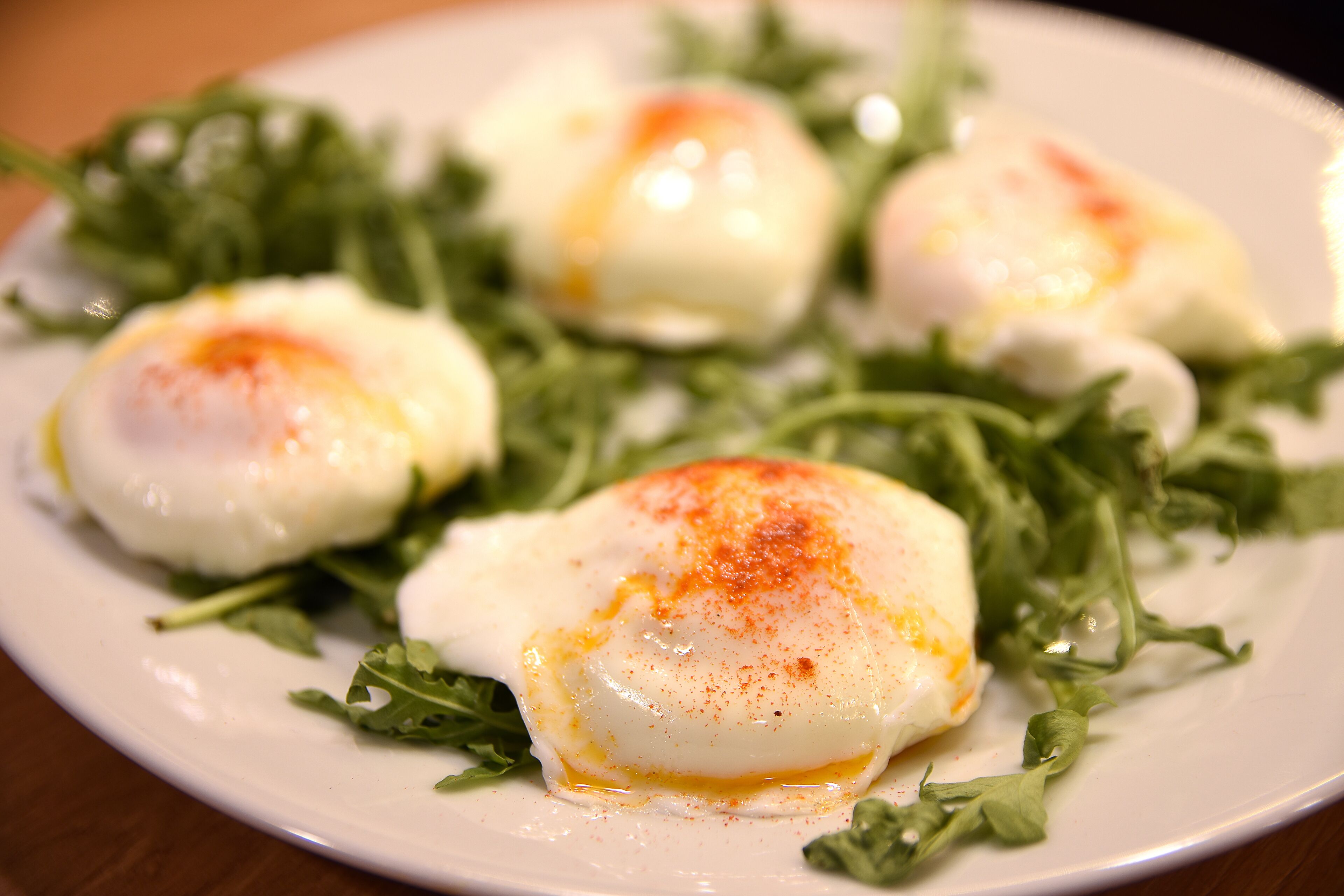 A plate of poached eggs with a sprinkle of paprika on top, served on a bed of arugula.