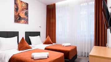 Habitació d'hotel amb dos llits, un quadre a la paret, una taula de nit amb una cadira i una finestra amb cortines.