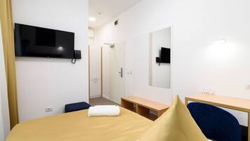A hotel room with a bed, a desk, a chair, a TV mounted on the wall, and a mirror.