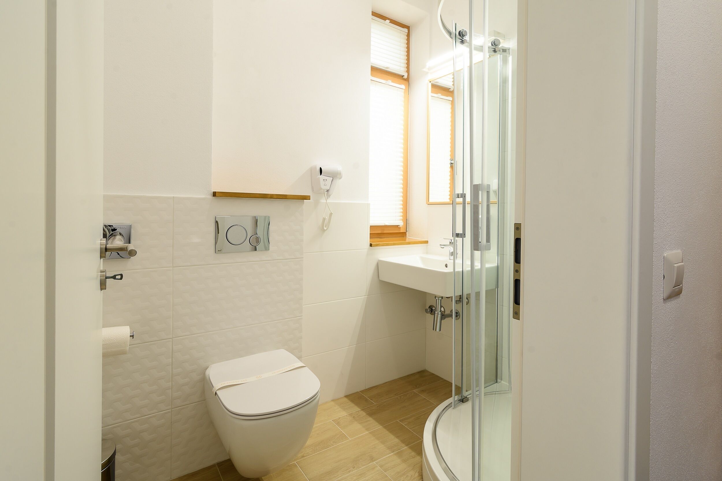 A bathroom with a toilet, a sink, a glass shower enclosure, and a hand dryer.