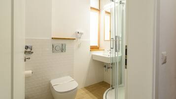 A bathroom with a toilet, a sink, a glass shower enclosure, and a hand dryer.