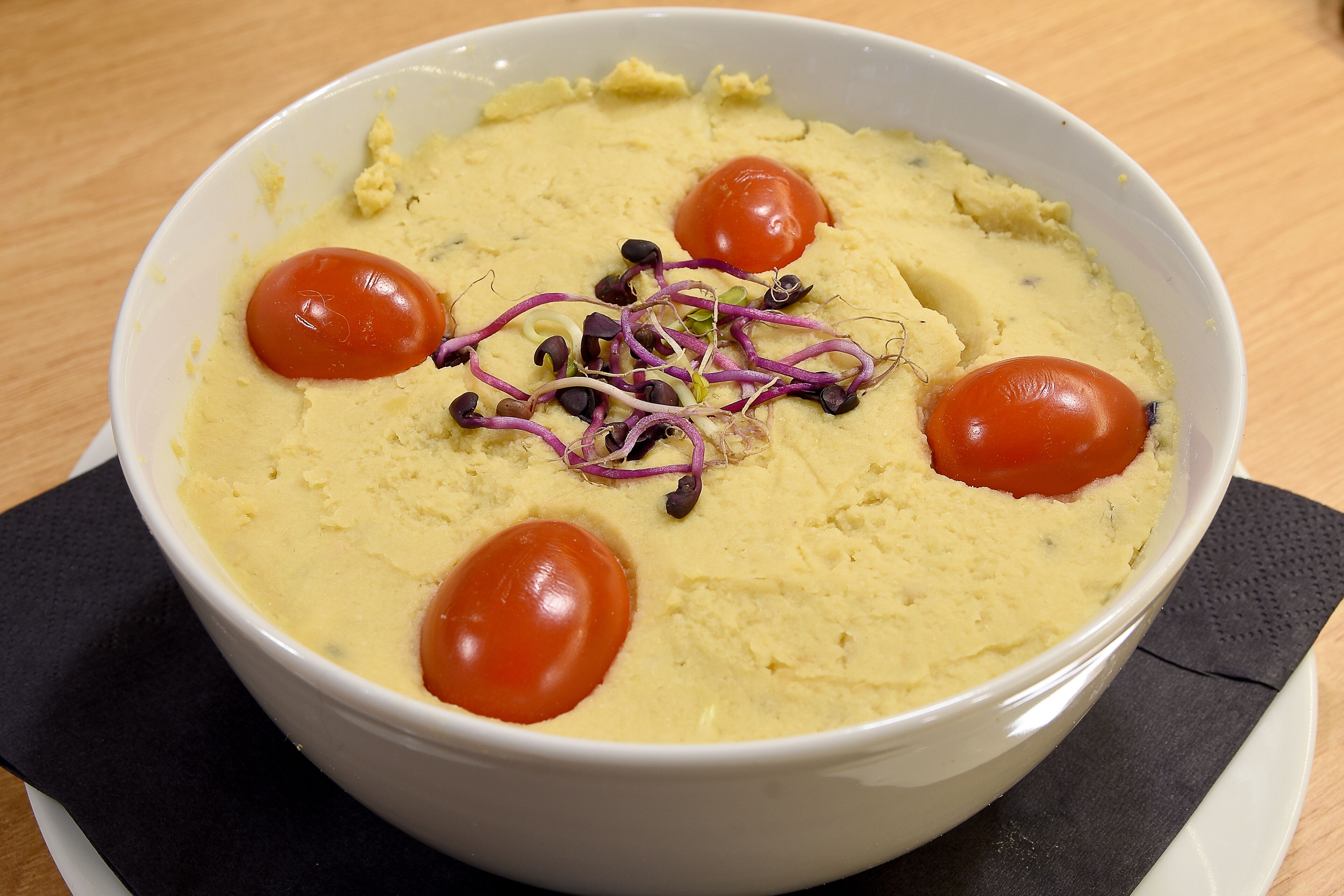 A bowl of food with a creamy texture, garnished with sprouts and cherry tomatoes.