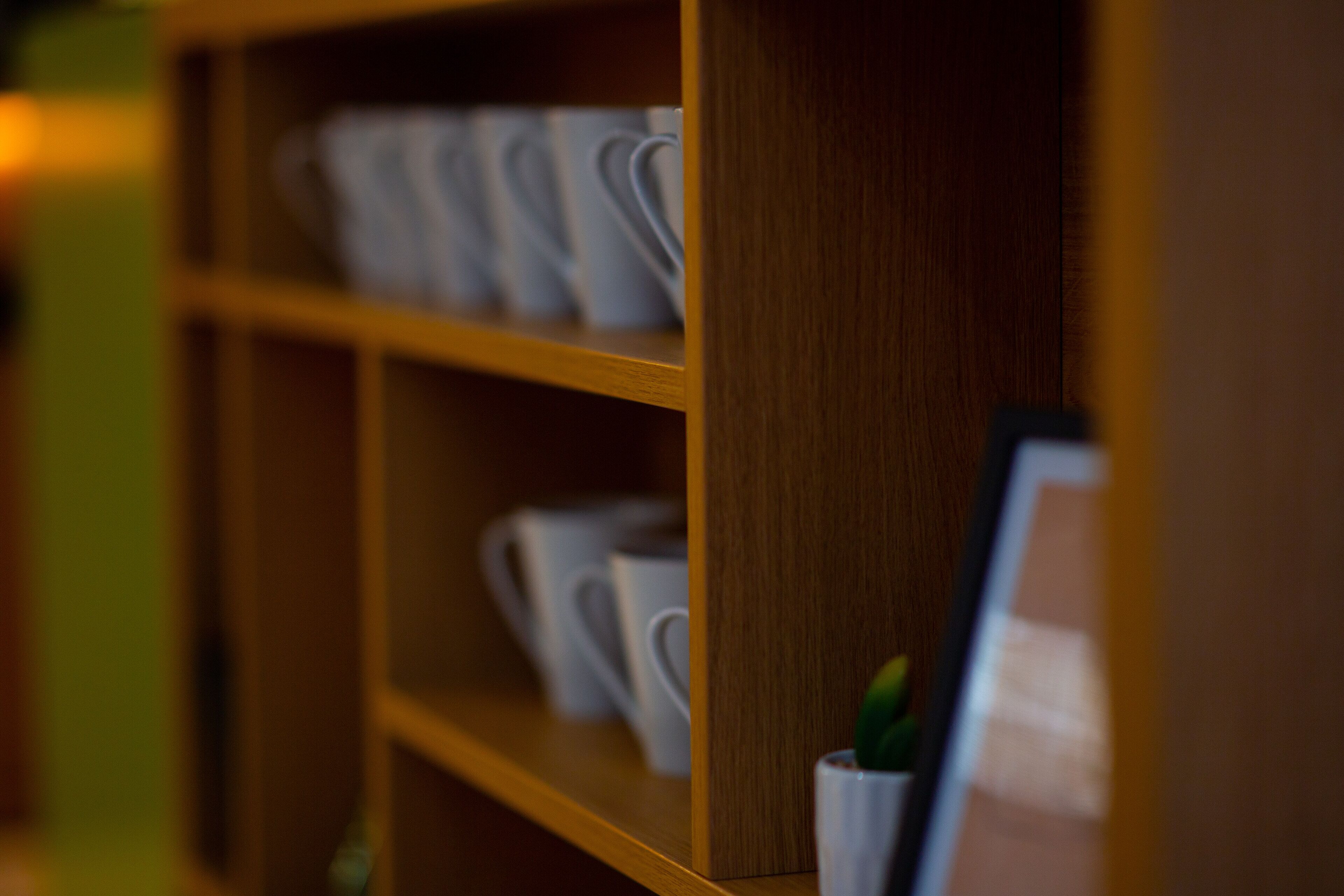 A wooden shelf with white cups and a small potted plant.