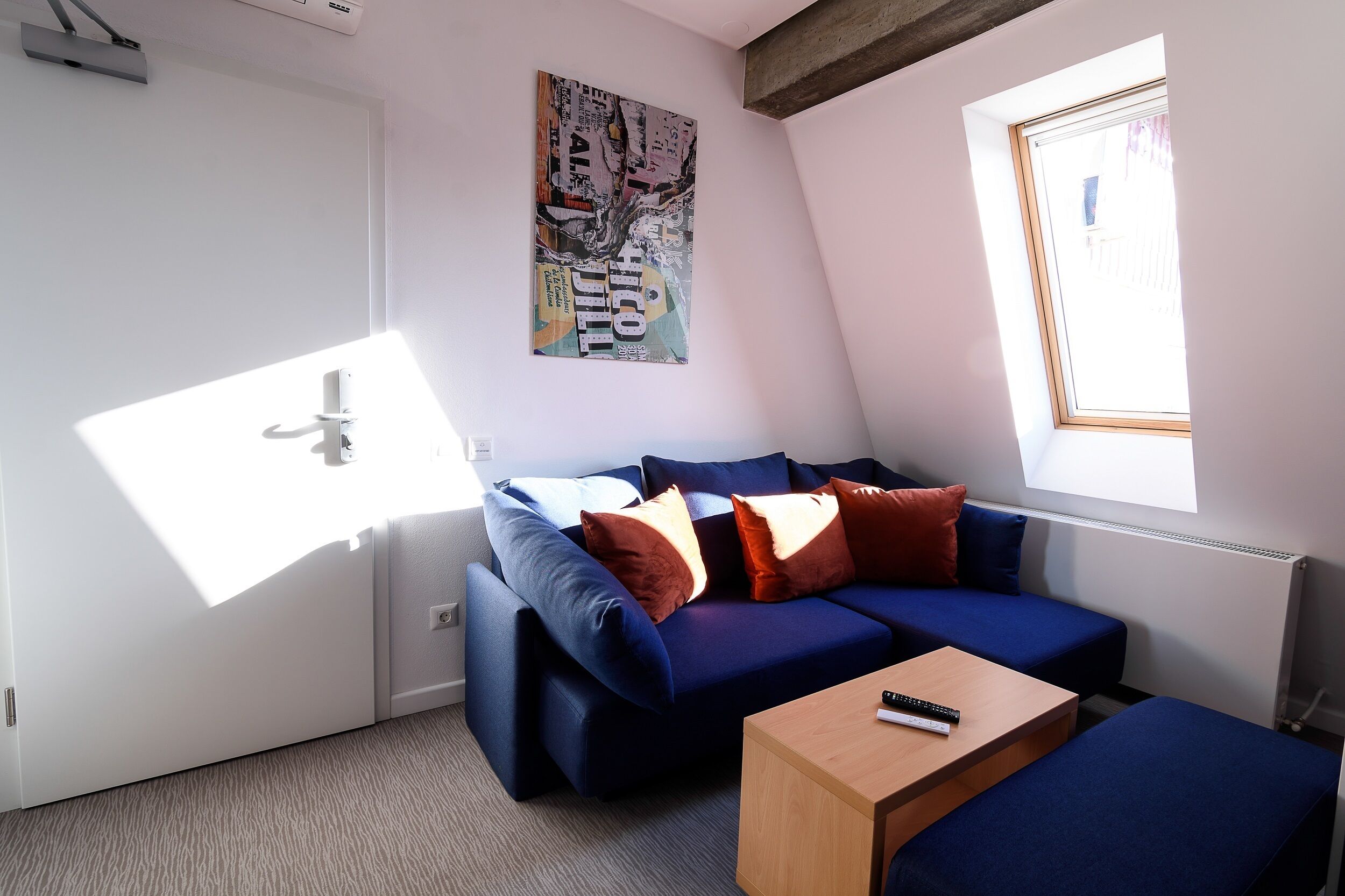 A modern, compact room with a blue sofa, a wooden coffee table, and a window with a view.