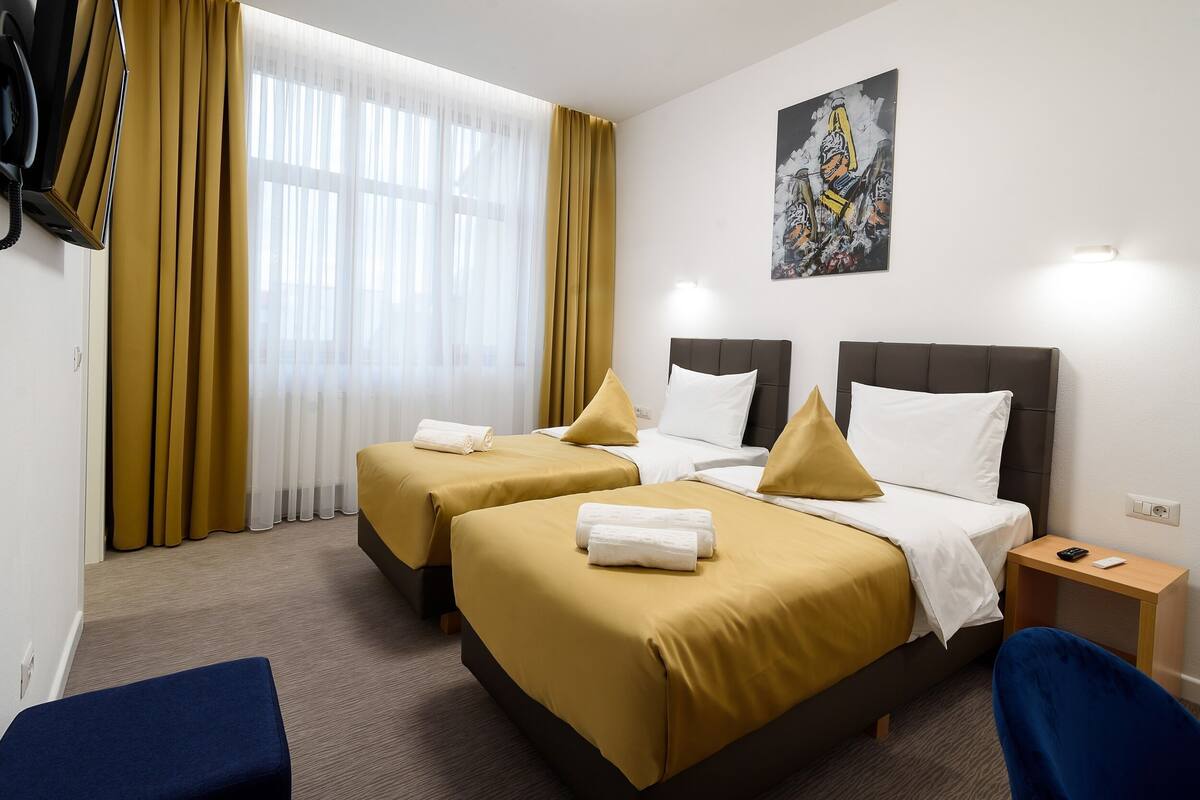 A hotel room with two beds, a small table, a chair, and a painting on the wall.