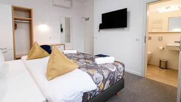 A hotel room with a bed, a TV, a mirror, and a bathroom visible through an open door.