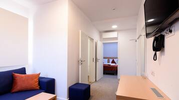 Habitación de hotel con un sofá azul, una mesita de madera, un otoman azul, cama con ropa de cama roja y un teléfono de pared.