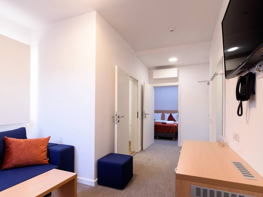 Habitación de hotel con un sofá azul, una mesita de madera, un otoman azul, cama con ropa de cama roja y un teléfono de pared.