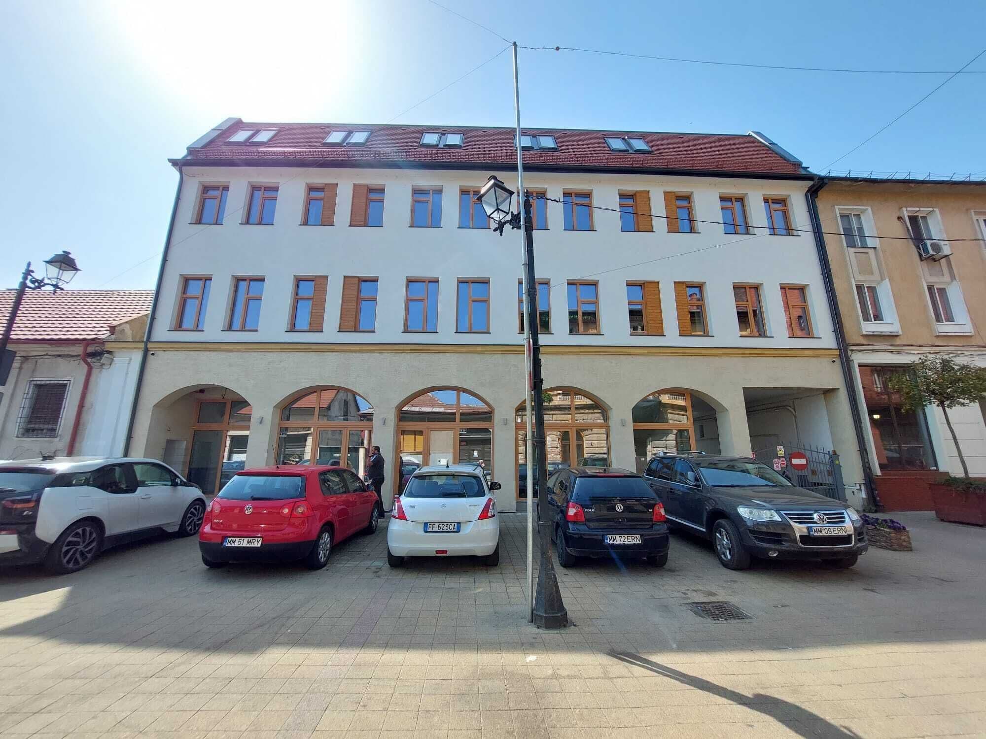 En byggnad med flera våningar, framför vilken en rad parkerade bilar står.