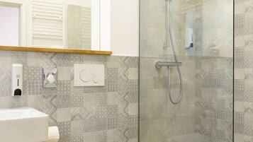 A modern bathroom with a glass shower enclosure, a toilet, and a sink with a soap dispenser.