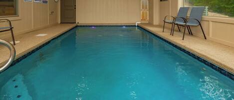 An indoor swimming pool with a clear water view, a pool ladder, and two lounge chairs by the window.