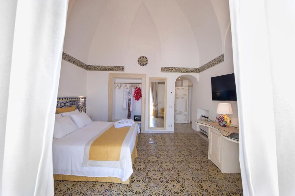 A hotel room with a bed, a desk, a mirror, and a TV.