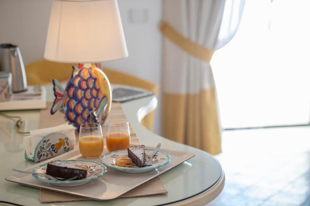 A breakfast table with a pineapple-shaped lamp, a glass of orange juice, and plates of food including a slice of cake and a pastry.