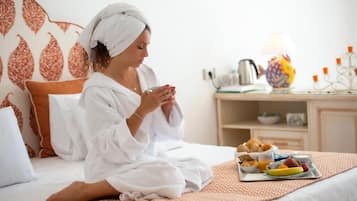 Una persona sentada en una cama con una bandeja de alimentos para el desayuno, una tetera y un pez decorativo en la mesita de noche.