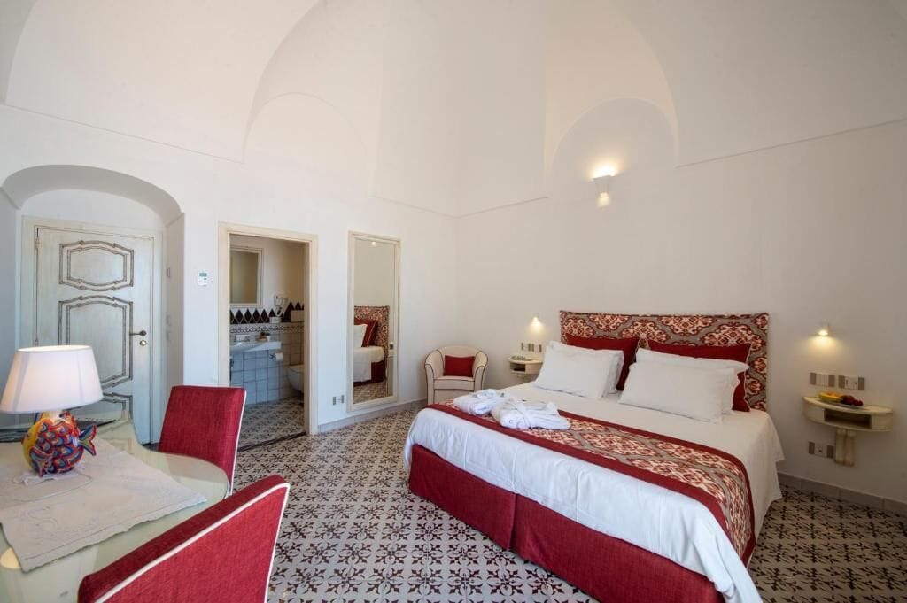 A hotel room with a large bed, a chair, a desk with a lamp, and a mirror.