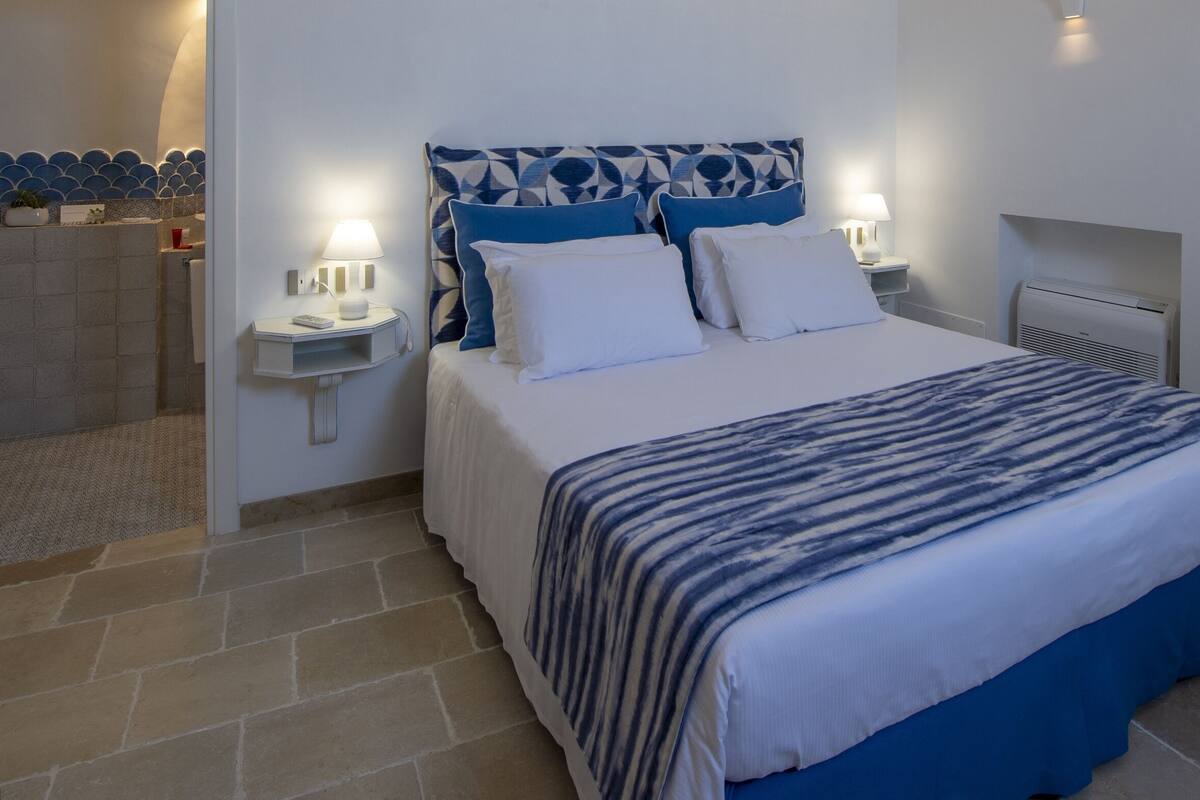 A bedroom with a bed, bedside tables, a nightstand, a wall-mounted heater, and a door with decorative molding.