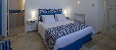 A bedroom with a bed, bedside tables, a nightstand, a wall-mounted heater, and a door with decorative molding.