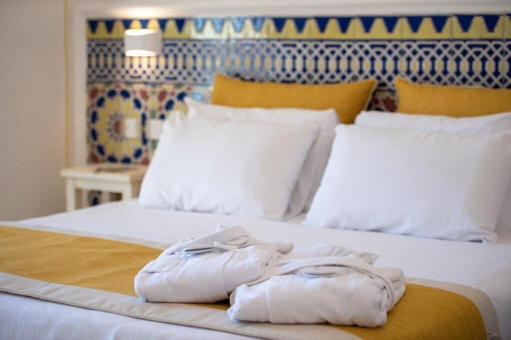 Una cama bien hecha con sábanas blancas, dos almohadas y un par de toallas dobladas sobre la cama.