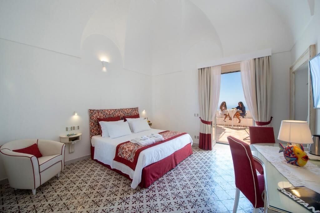Habitació d'hotel amb un llit gran, un escriptori amb una làmpada, una cadira i vista al balcó.