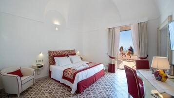 Habitació d'hotel amb un llit gran, un escriptori amb una làmpada, una cadira i vista al balcó.