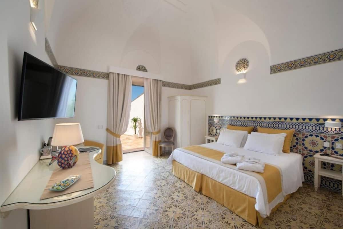 A hotel room with a bed, a TV, a desk with a lamp, and a view of the outdoors.