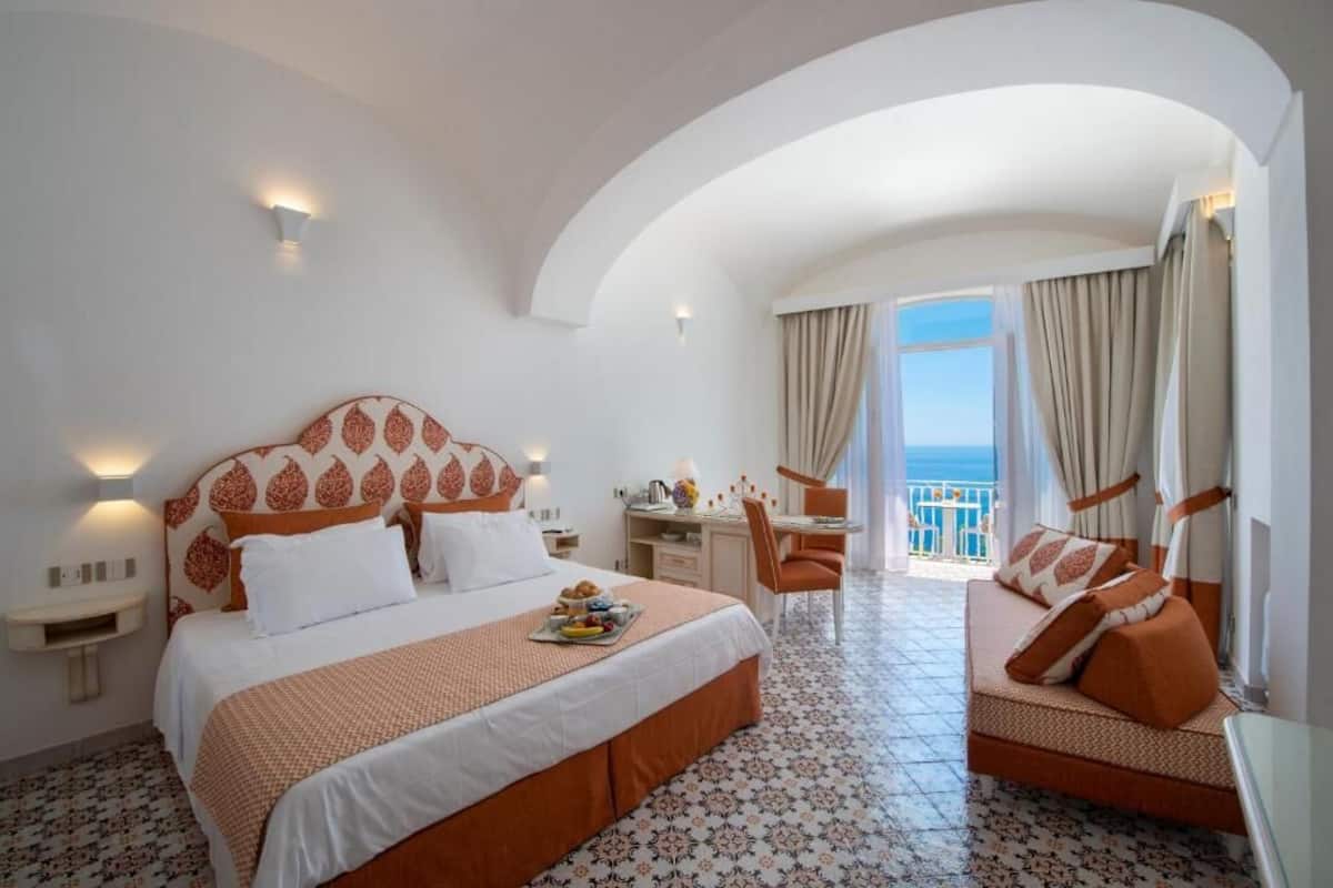 A hotel room with a large bed, a desk, and a view of the sea.