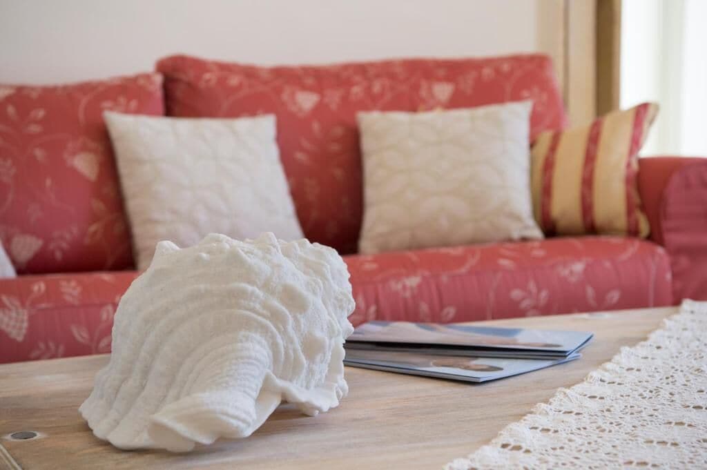 Ein ordentlich eingerichteter Wohnbereich mit einem roten Sofa, verziert mit gemusterten Kissen, einer weißen Strickdecke und einer Spitzen Tischläufer.