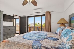 Une chambre dotée d’un grand lit, d’une télévision, d’un ventilateur de plafond, d’un appareil de climatisation et offrant une vue sur un balcon aménagé avec du mobilier d’extérieur.