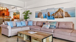 Een woonkamer met een beige bank, gestreepte kussens, een houten salontafel en wanddecoratie met kustlandschappen.