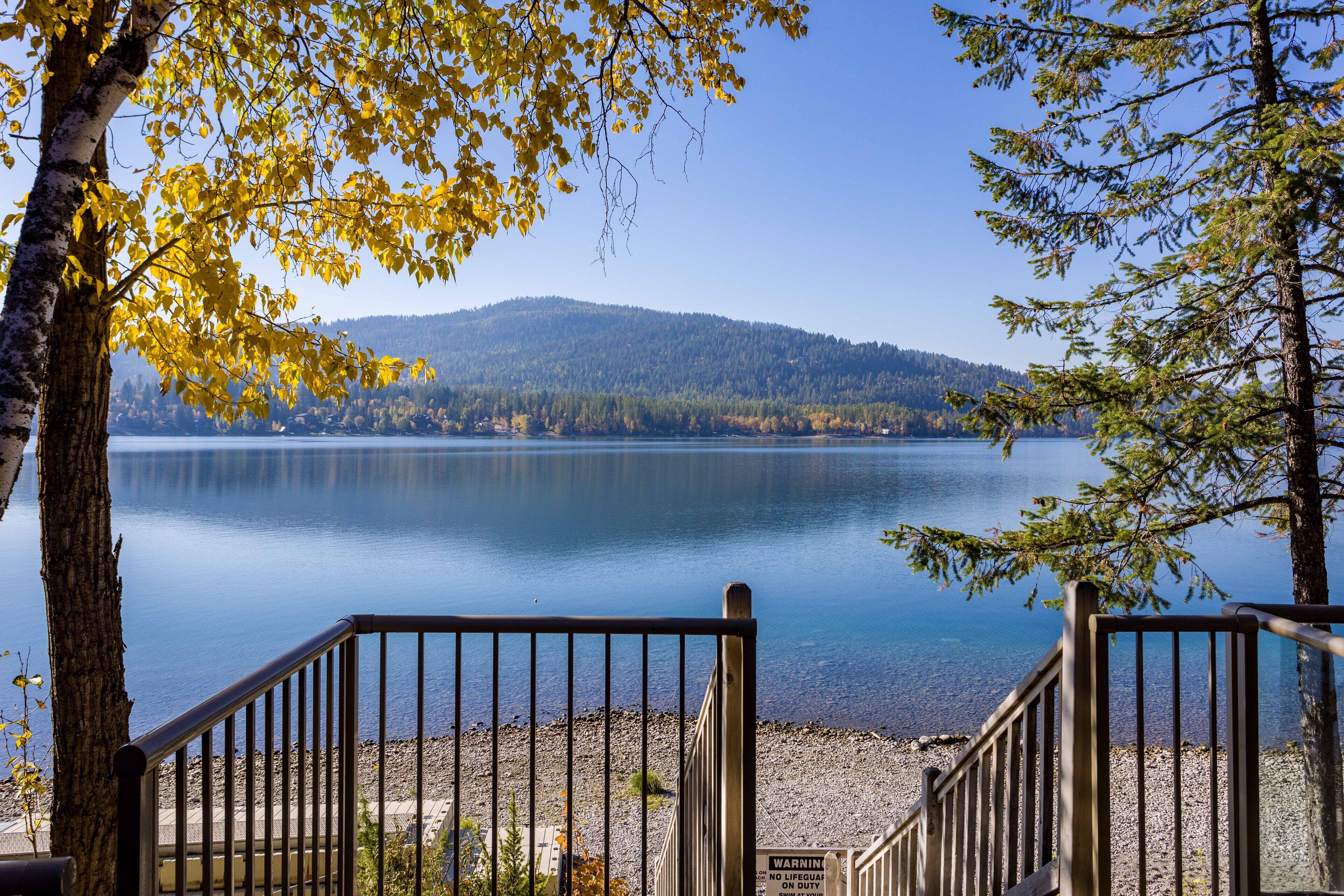 A lake with a forested hill in the background, a wooden deck, and a metal railing.