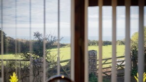 Uitzicht door een houten hek met een stenen muur en een houten omheining, dat uitkomt op een groen veld en bomen.