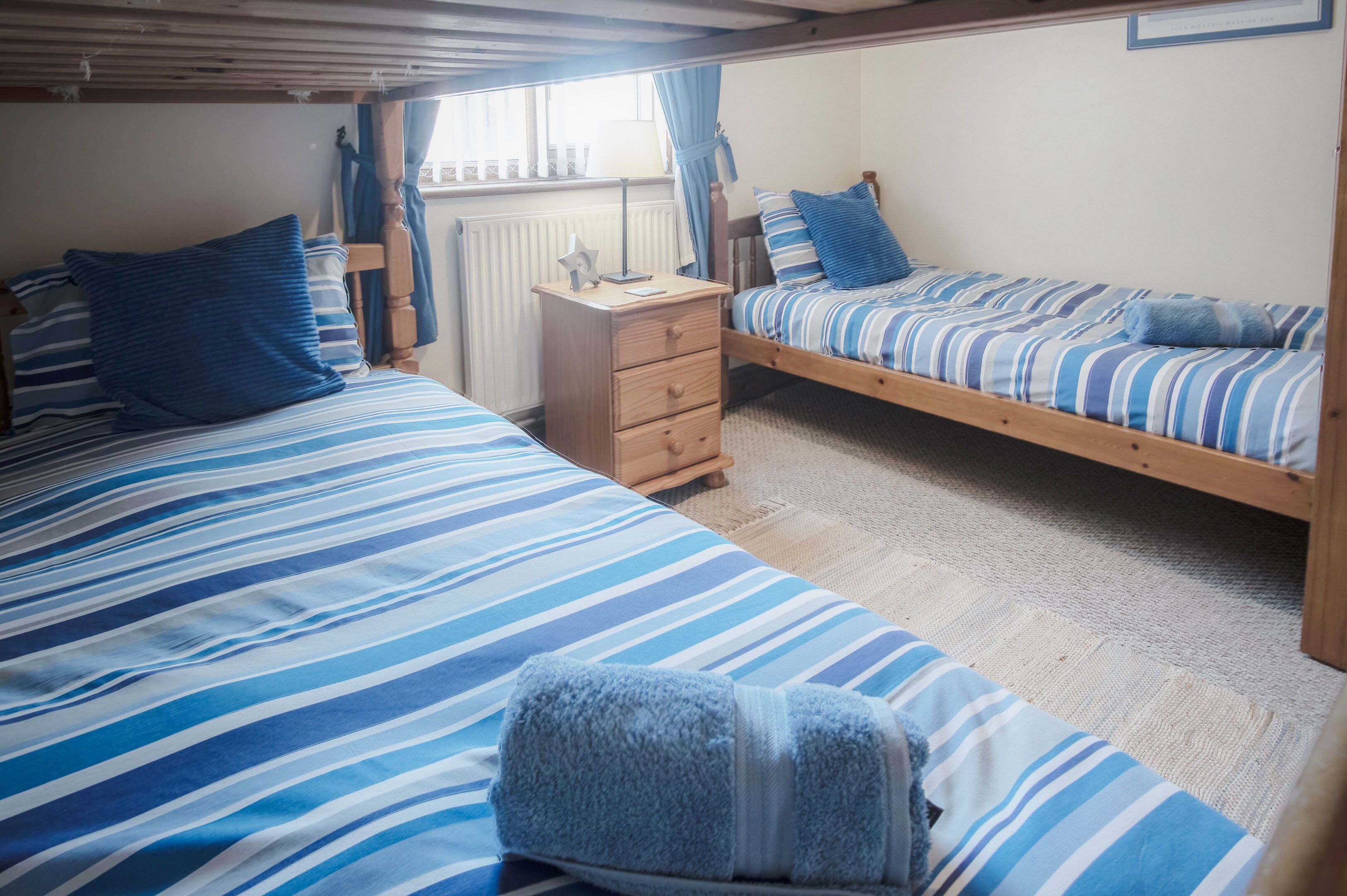 A room with two single beds, a wooden dresser, and a window with curtains.