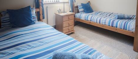 A room with two single beds, a wooden dresser, and a window with curtains.