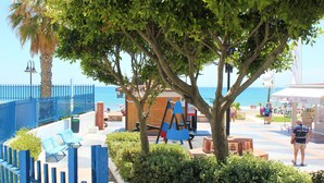 Une promenade en bord de mer agrémentée d’une clôture bleue, de bancs et d’une aire de jeux.