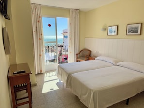 Ein Hotelzimmer mit zwei Betten, einem kleinen Tisch, einem Stuhl, einem Balkon mit Geländer und Meerblick.