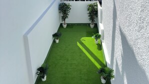 Une cour avec une pelouse artificielle, des plantes en pot et un mur blanc.