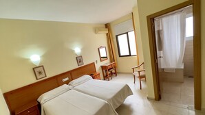 Une chambre d’hôtel avec deux lits, un bureau, une chaise, une fenêtre avec des rideaux et une porte.