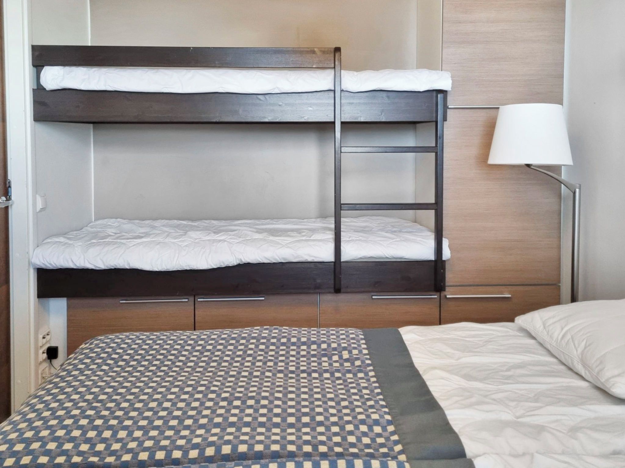 A bunk bed with a ladder, a bedside table, a lamp, and a patterned rug.