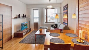 Una sala de estar moderna con una mesa de comedor de madera, un sofá gris y un televisor sobre un mueble de madera.