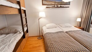 Una habitación de hotel con una cama litera, dos camas individuales, una lámpara de pie y un cuadro en la pared.