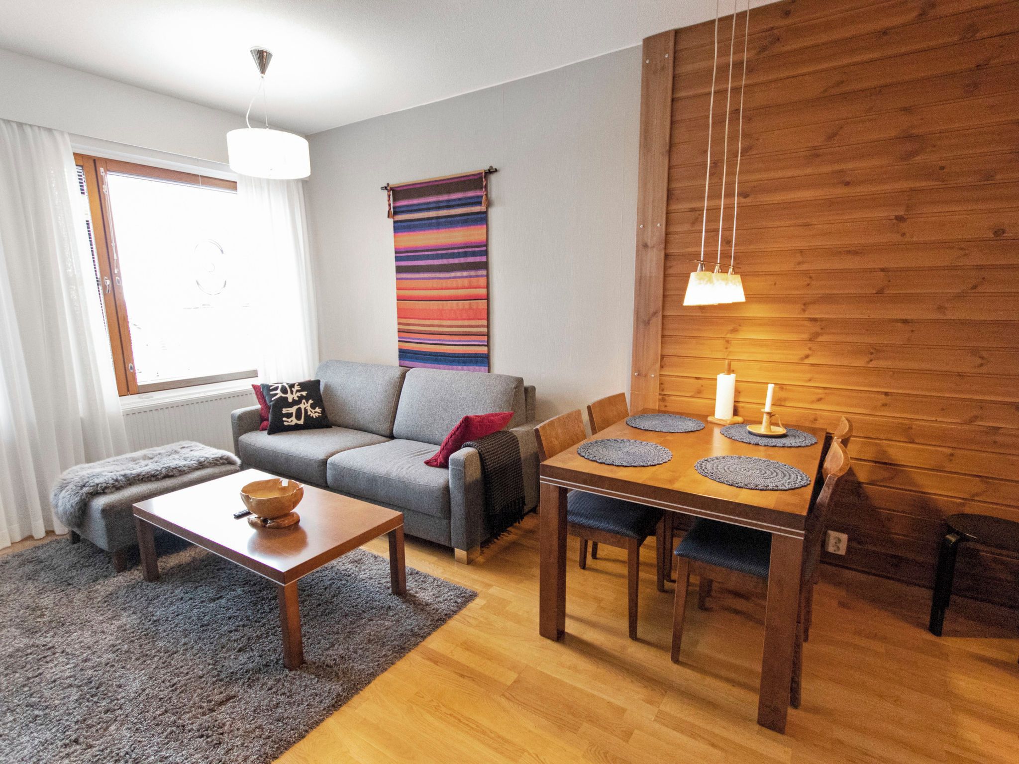 Un salon avec un canapé gris, une table à manger en bois avec quatre chaises, une table basse et un mur en bois.