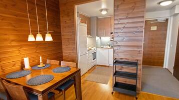 Ett modernt kök med träpanel på väggarna, en matplats med ett träbord och stolar samt en liten köksö.