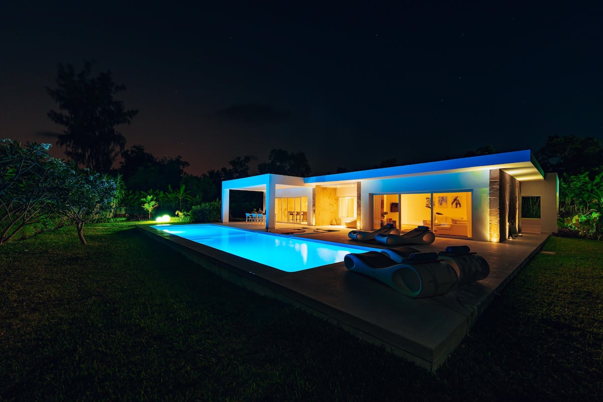 Ein modernes Haus mit Pool, Terrasse und gut beleuchtetem Innenraum.