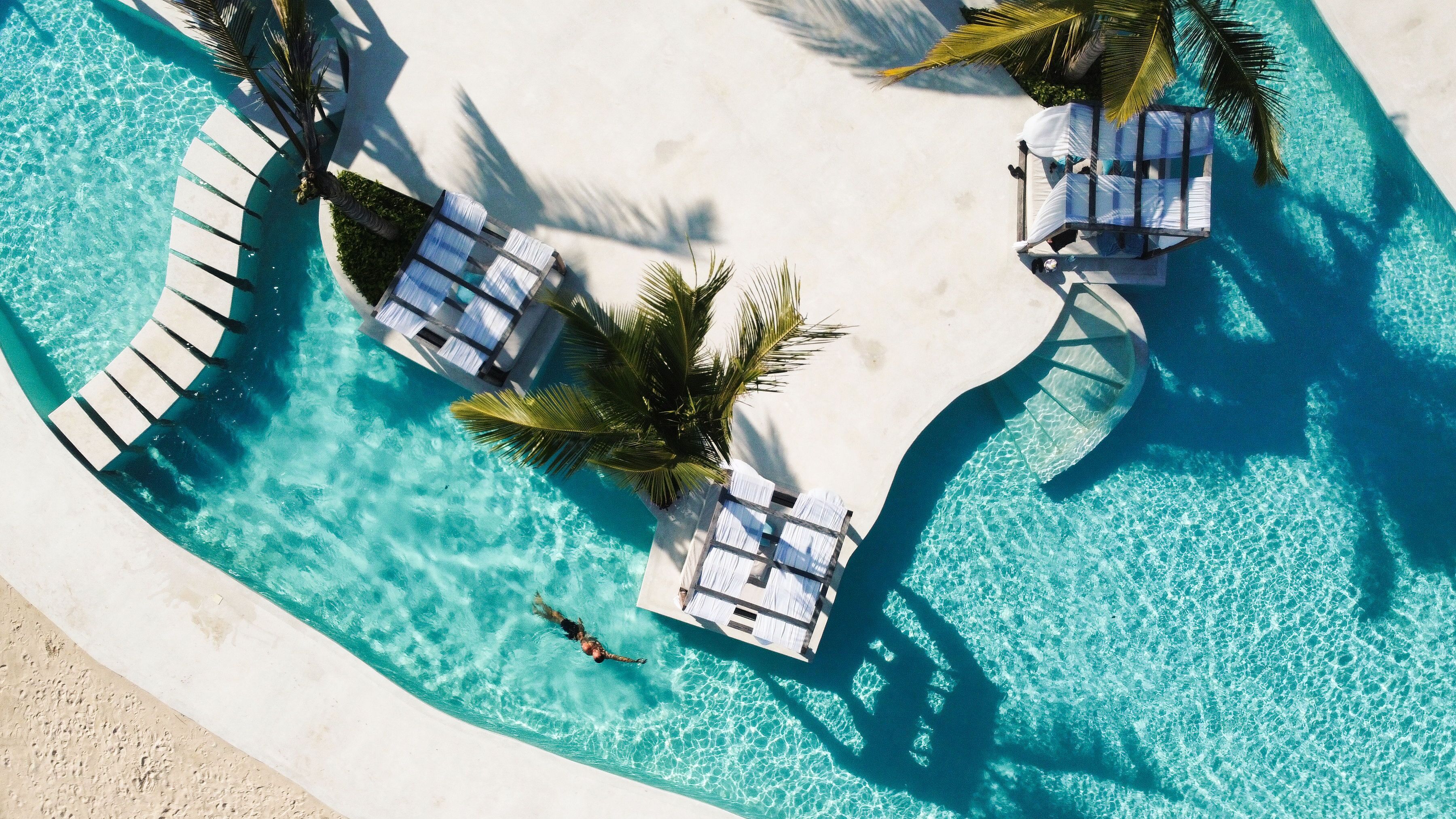 An aerial view of a pool area with lounge chairs and palm trees.
