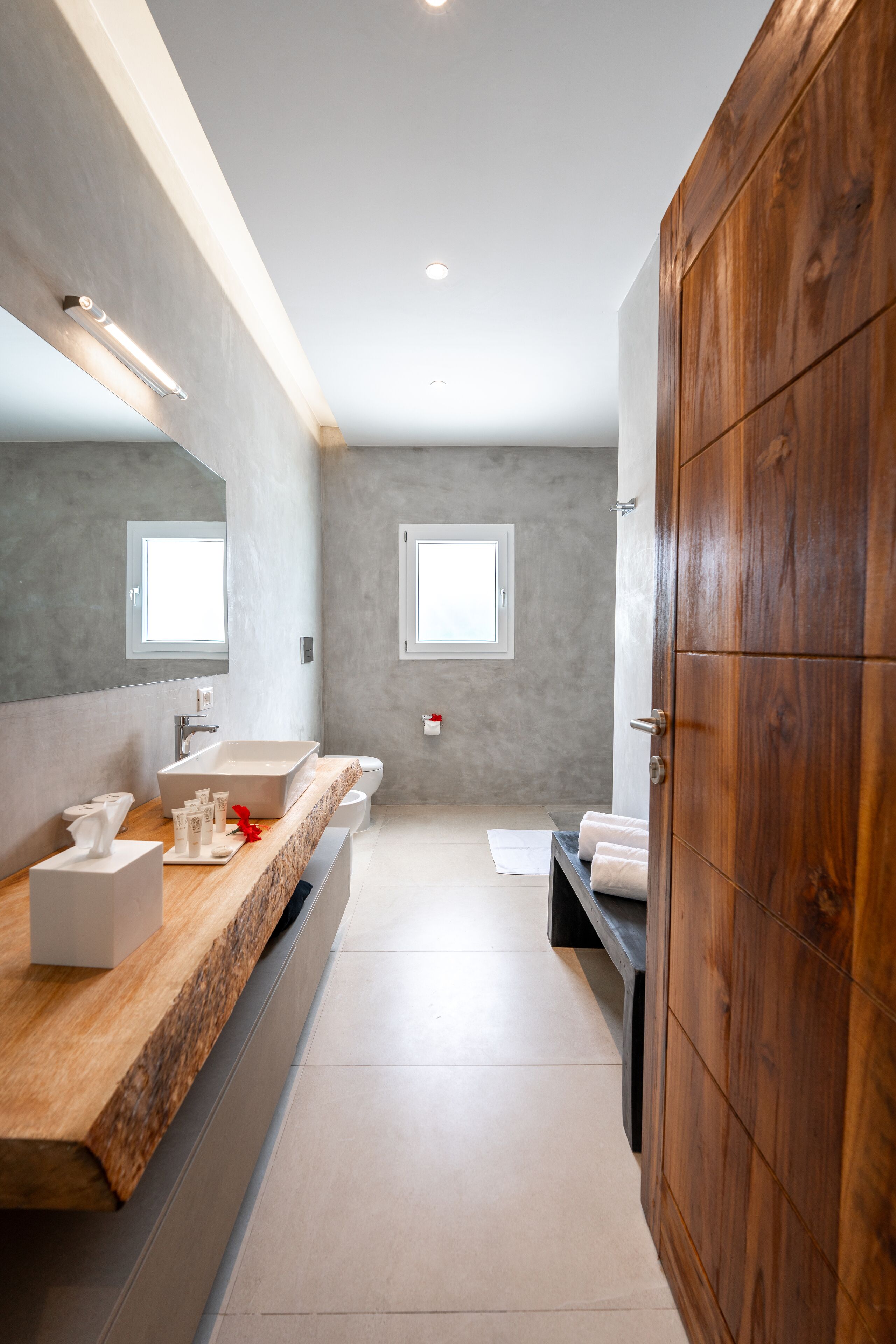 Un baño moderno con tocador de madera, un espejo grande y una ventana que proporciona luz natural.