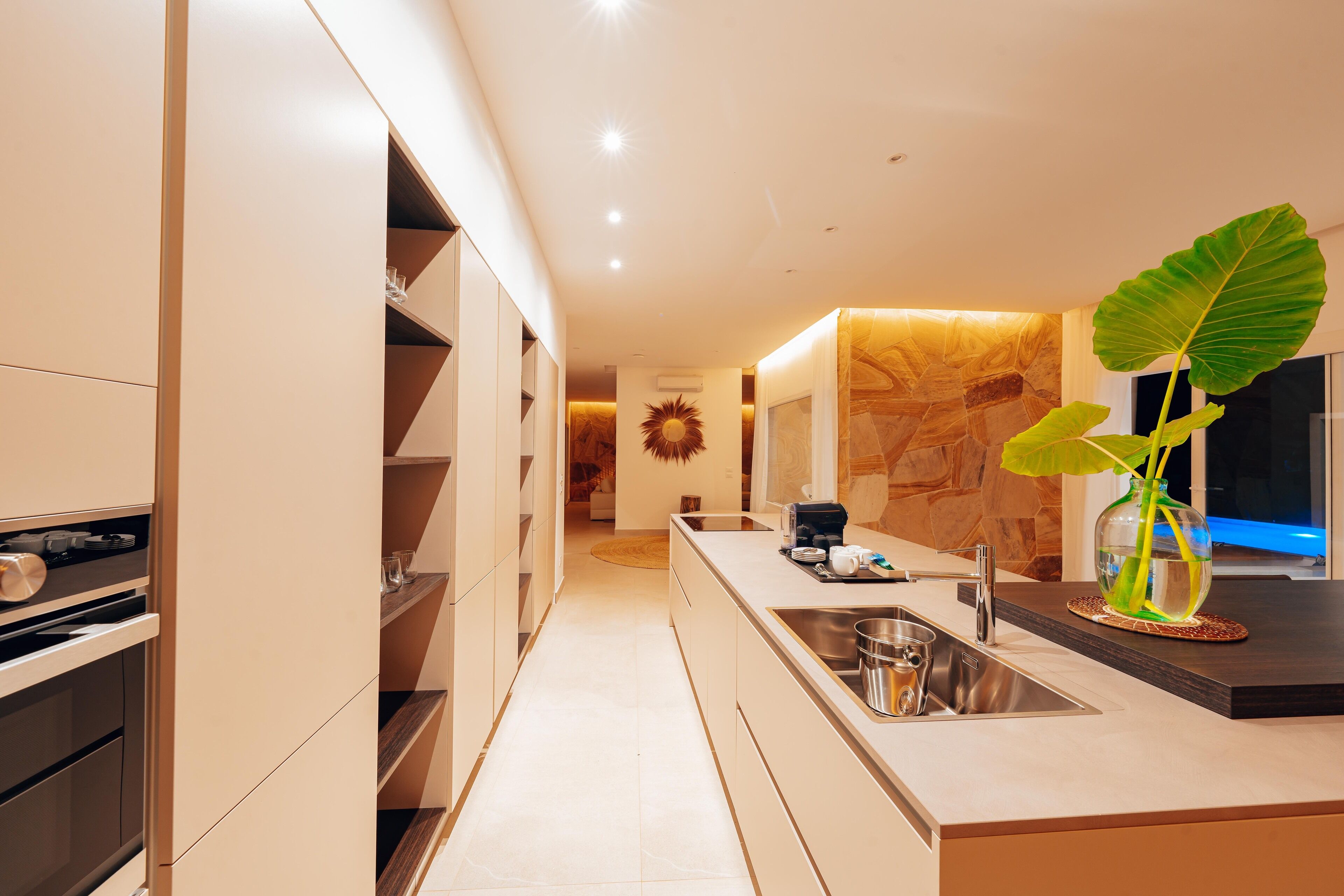 A modern kitchen with built-in appliances, a large island with a sink, and a decorative plant.