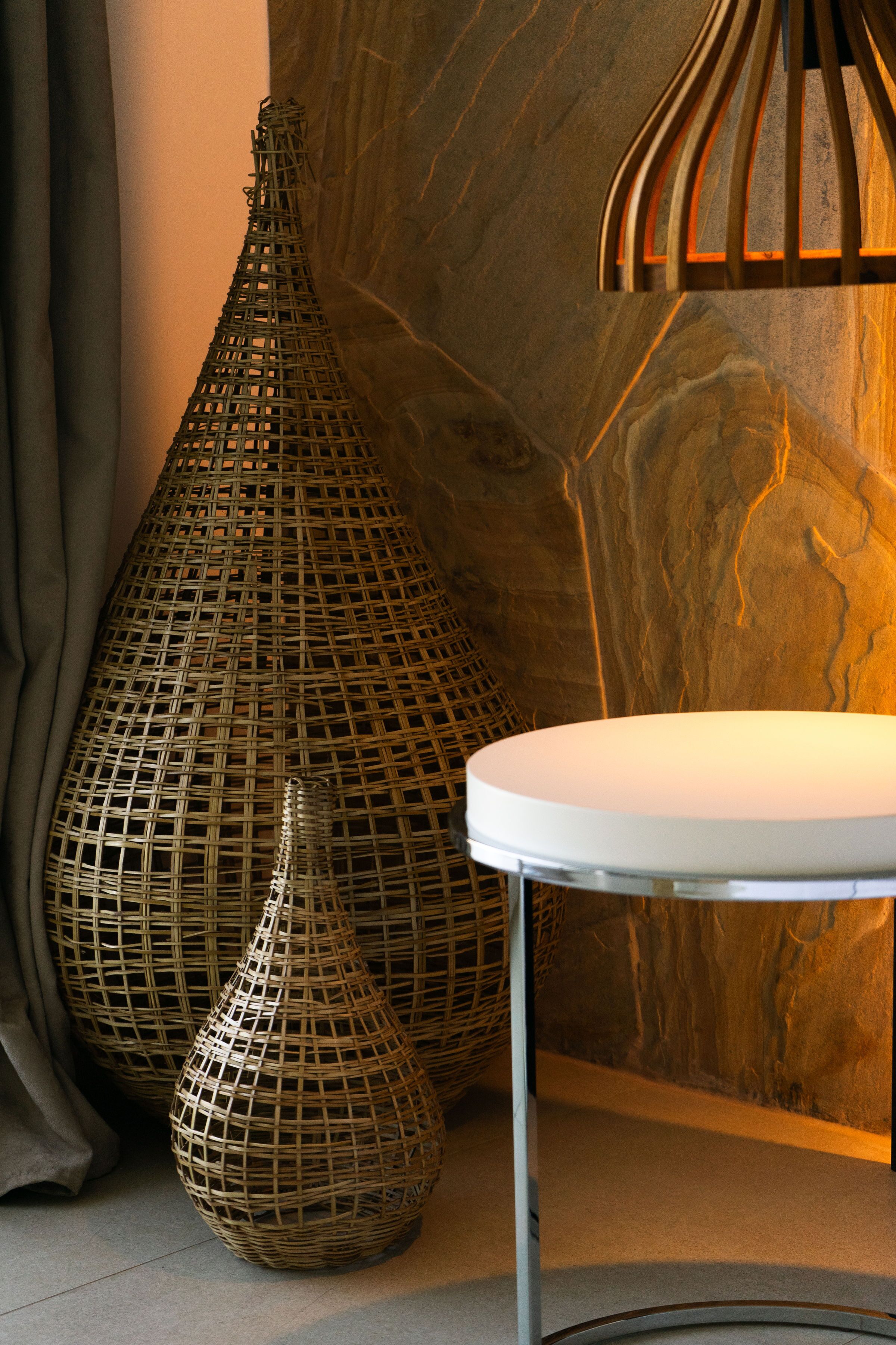 Una habitación con una mesa redonda blanca, dos grandes jarrones tejidos y una pared de madera con textura similar al mármol.