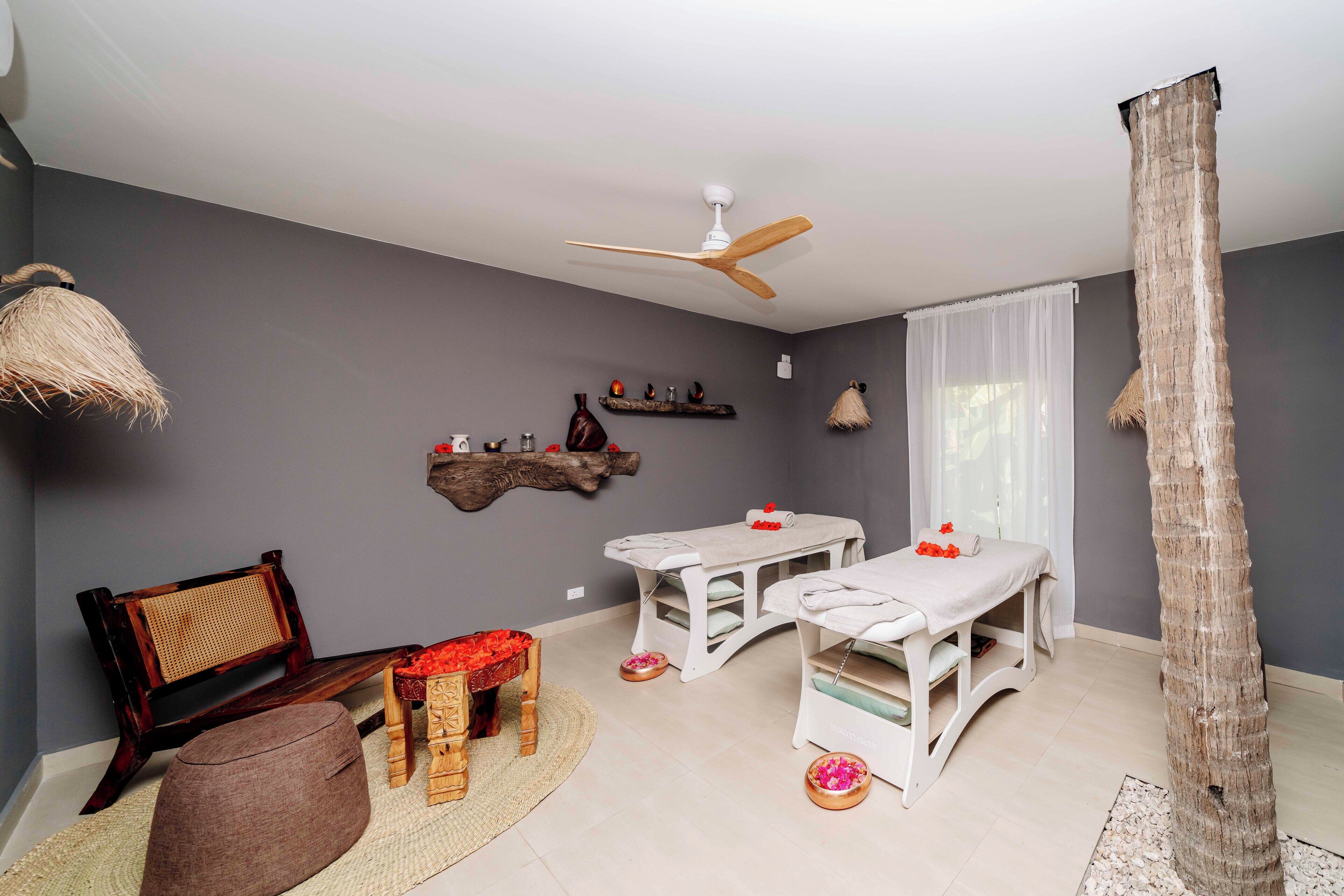 Een kamer met een plafondventilator, een houten bank, een massagetafel en een decoratieve boomstam.
